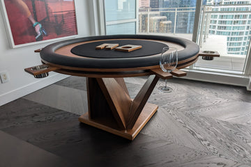 Wooden poker table with black felt top in a room with large windows showing a cityscape.