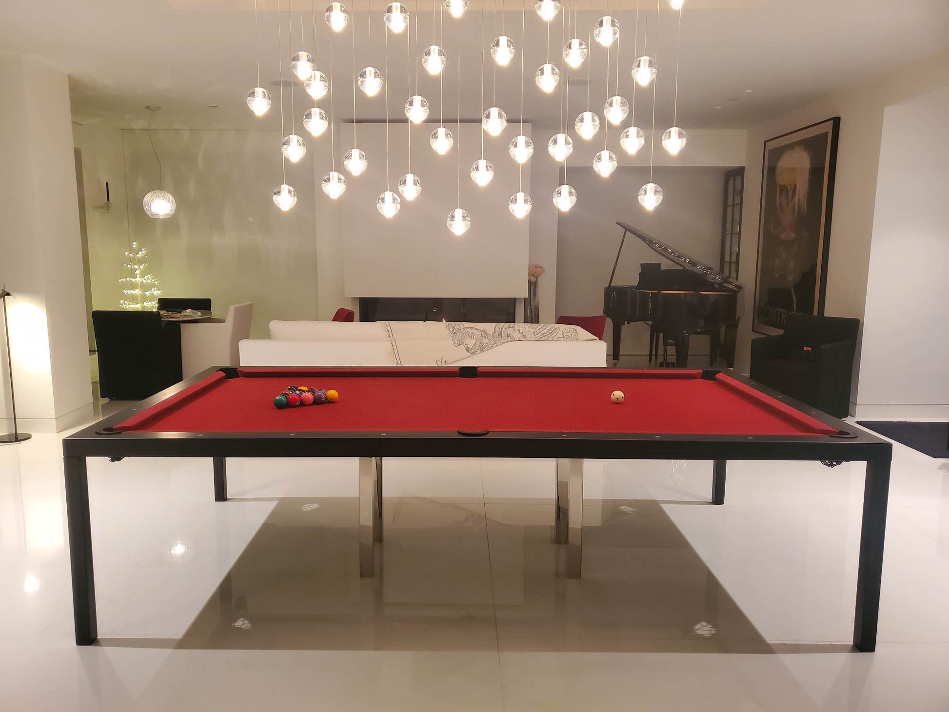 Modern pool table with red felt surface in a stylish room with chandelier and sofa.