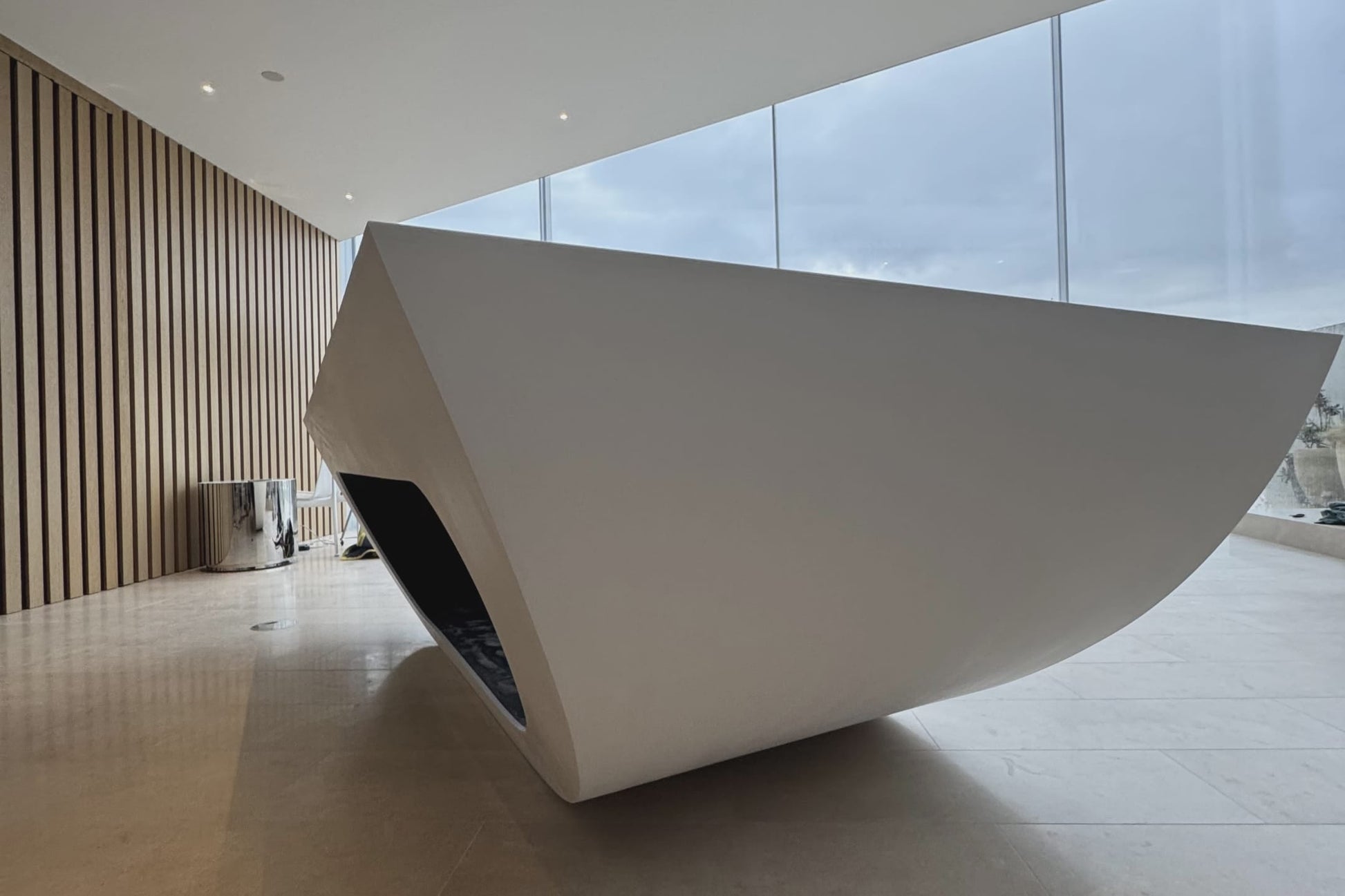 Modern white sculpture in a minimalist indoor setting with large windows.