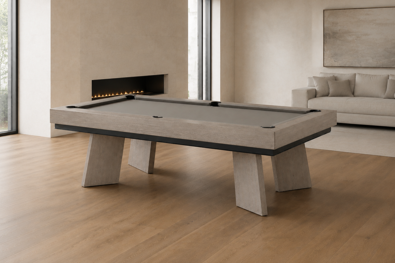 A modern pool table with a gray felt surface and light gray stone-like legs, positioned in a contemporary living room with wood floors, a fireplace, and a sofa in the background.