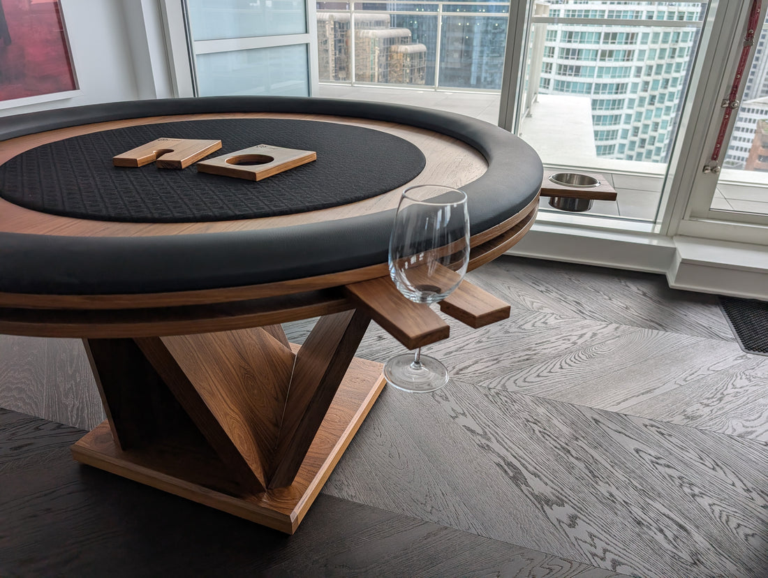 Wooden poker table with black felt top in a room with large windows showing a cityscape.