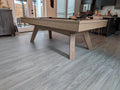 Wooden pool table in a room with large windows and modern decor.