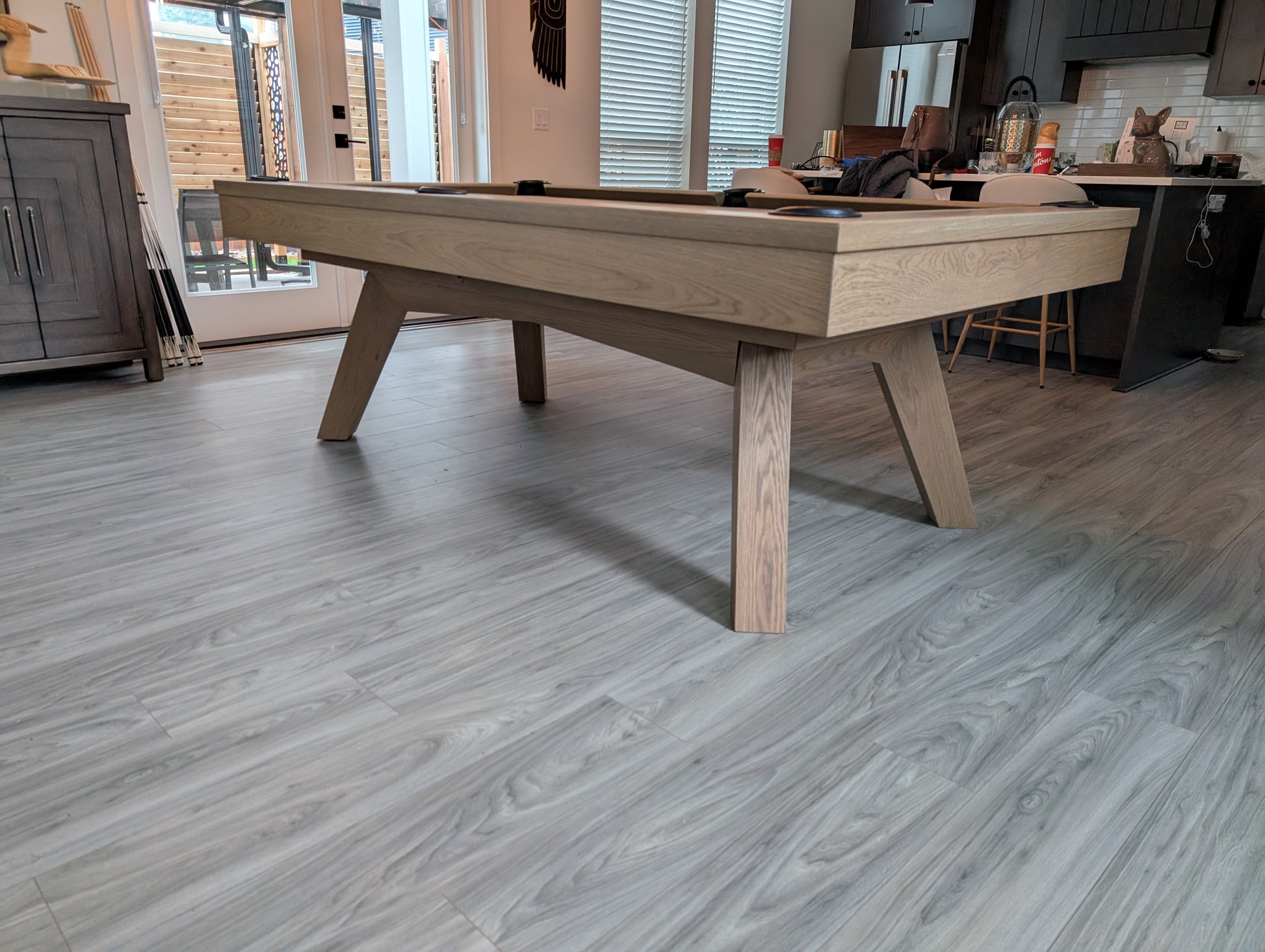 Wooden pool table in a room with large windows and modern decor.