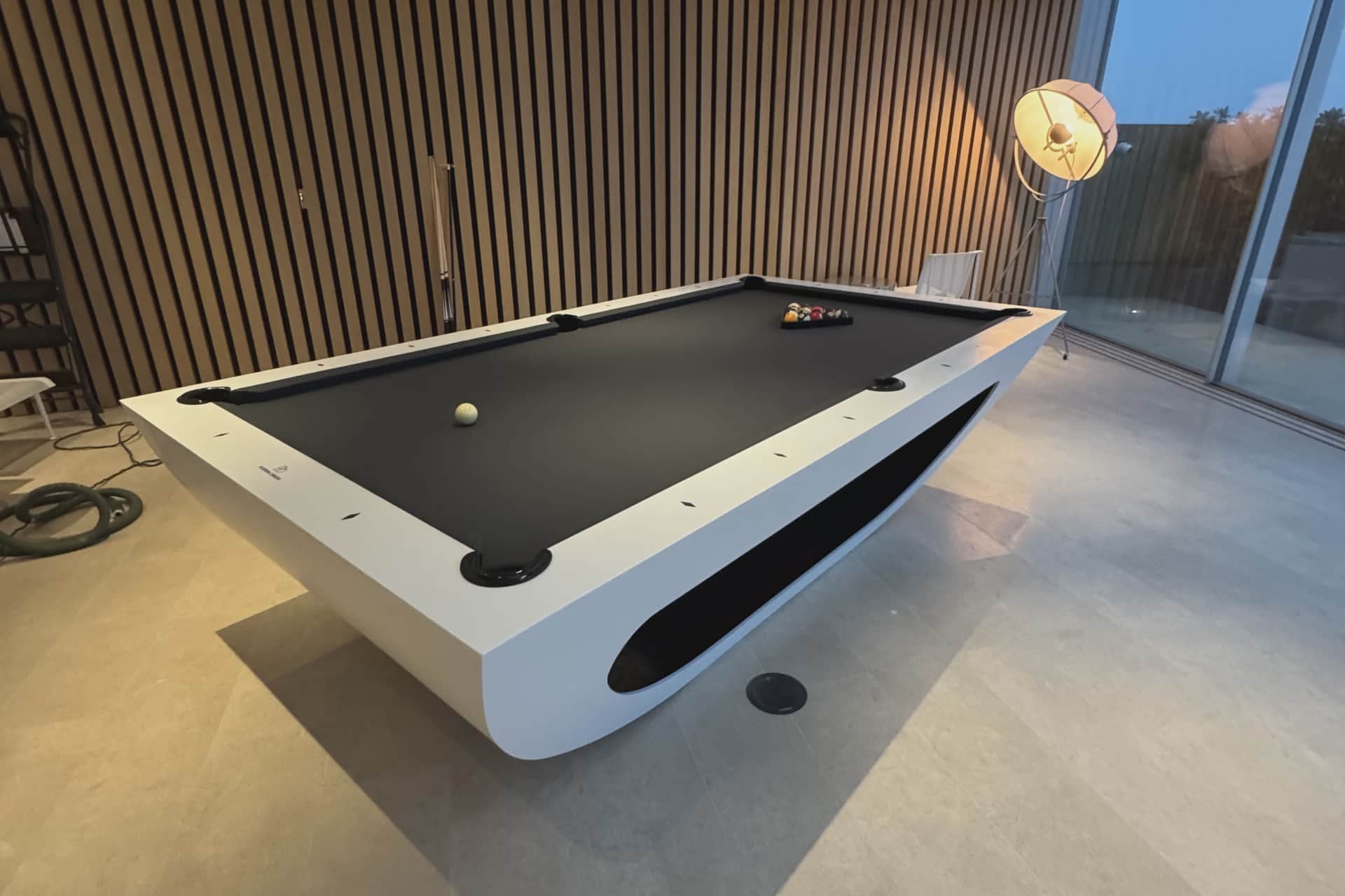 Modern pool table in a room with wooden paneling and a large window.